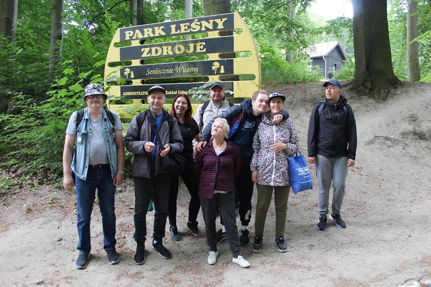 1.Grupa uczestników stojących na tle zieleni oraz tablicy z napisem „ Park Leśny Zdroje” D