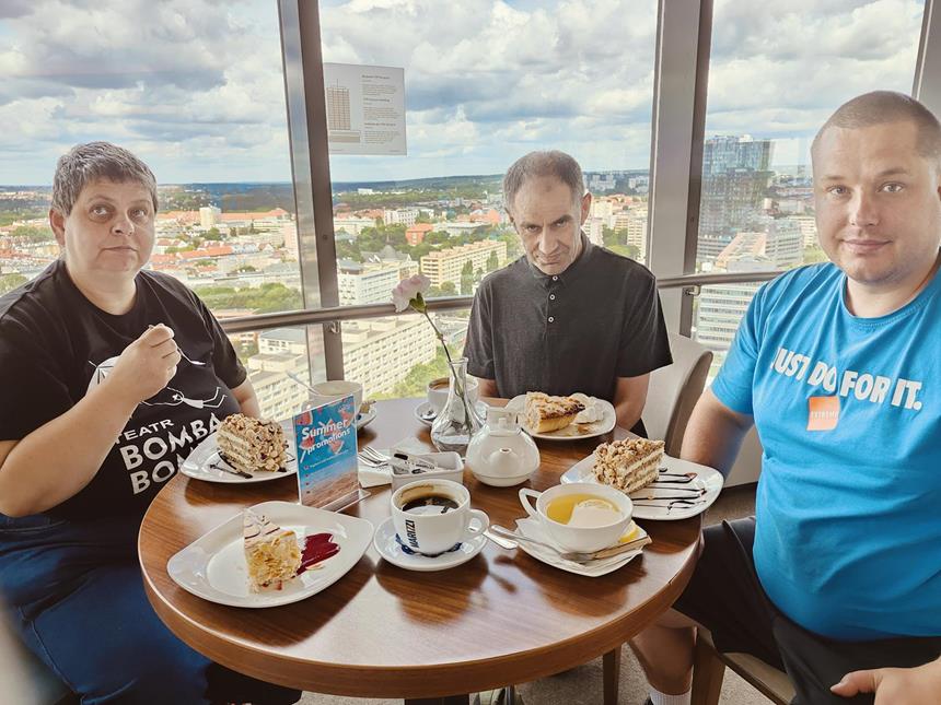 1.Uczesniczka oraz dwoje uczestników siedzący przy stole z kawą na tle panoramy szczecina D