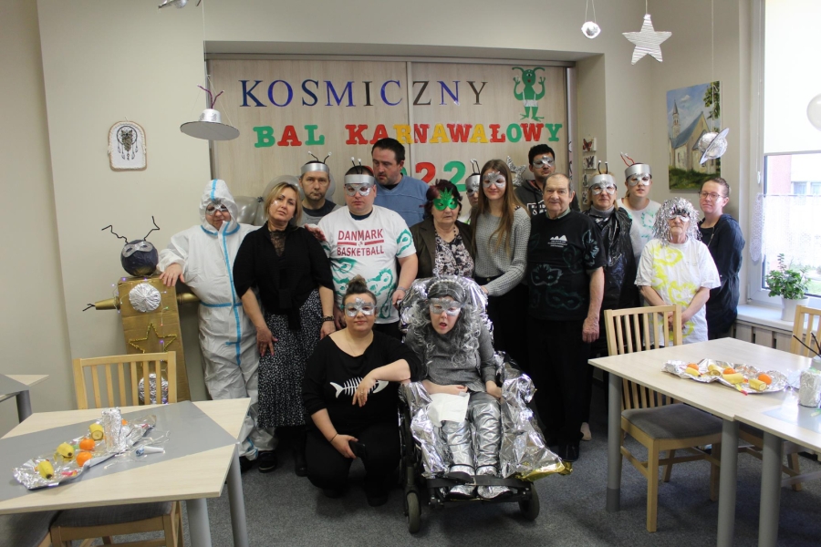 1 – Grupa Uczestników wraz z terapeutami pozują do zdjęcia na tle napisu.