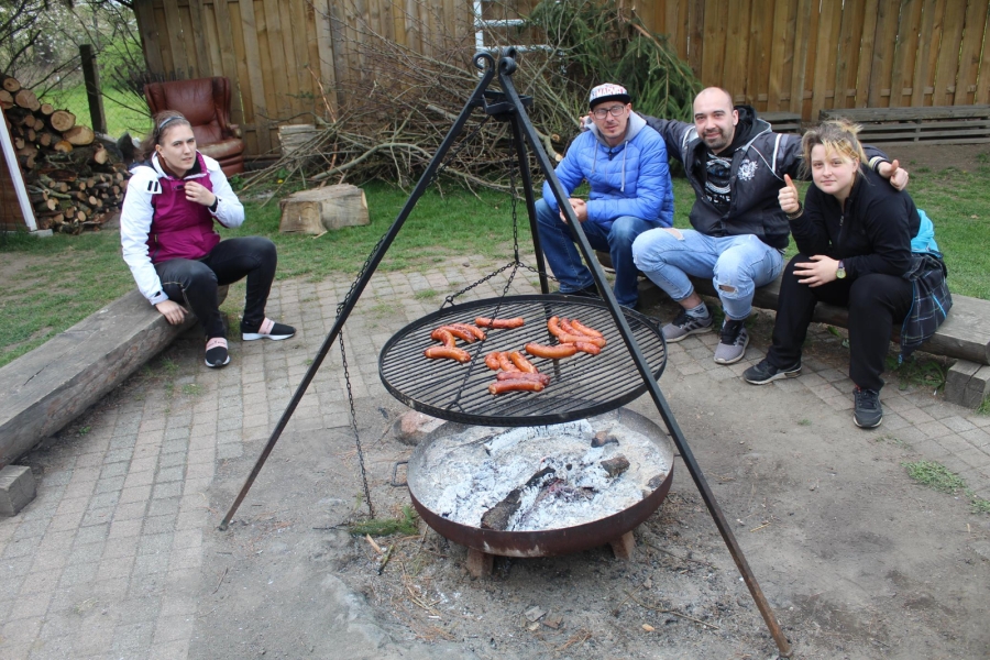 6 -  Uczestnicy pozują do zdjęcia na tle grilla z kiełbaskami.