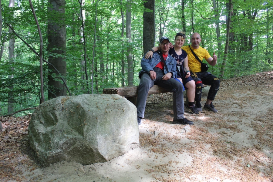 Uczestnicy siedzący na ławce pozują do zdjęcia przy kamieniu.