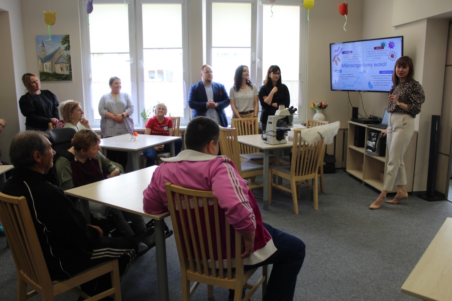 Uczestnicy słuchający wykładu pani profesor na temat mikroorganizmów.