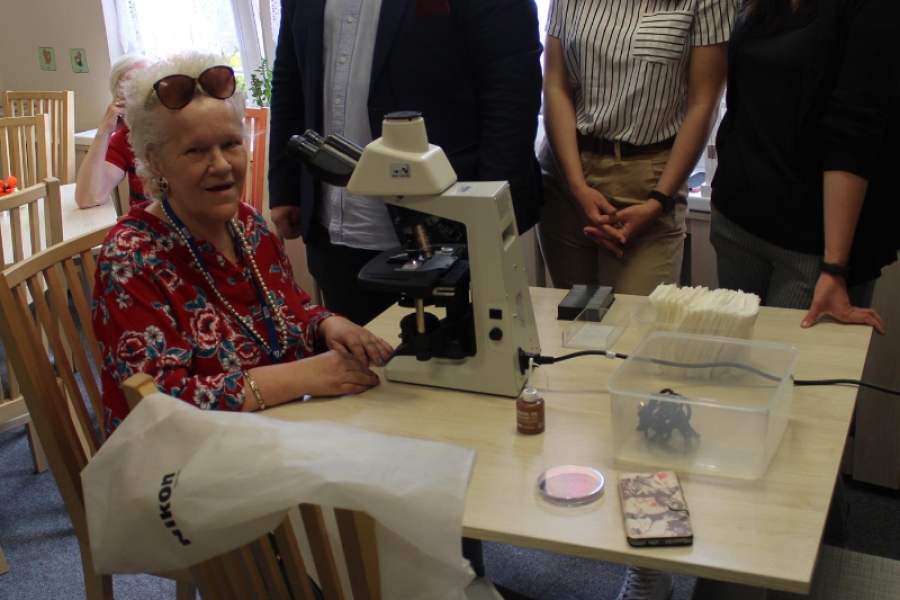 Uśmiechnięta Uczestniczka patrzy w mikroskop na tle gości.