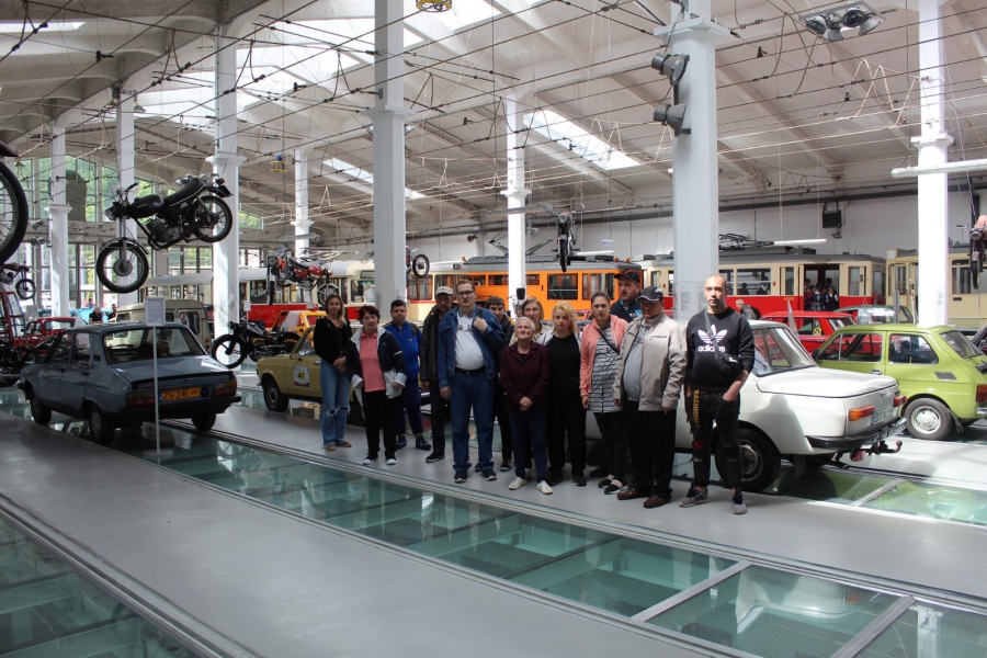 Uczestnicy pozujący do zdjęcia grupowego na tle pojazdów mechanicznych.