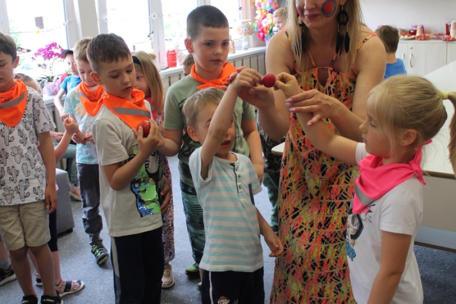 Pani pedagog podczas zabawy z warzywami trzymająca dzieci za ręce. 