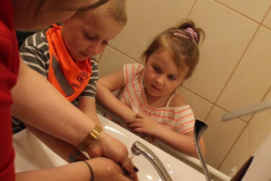 Opiekun medyczny wraz z dziećmi myją dłonie. 