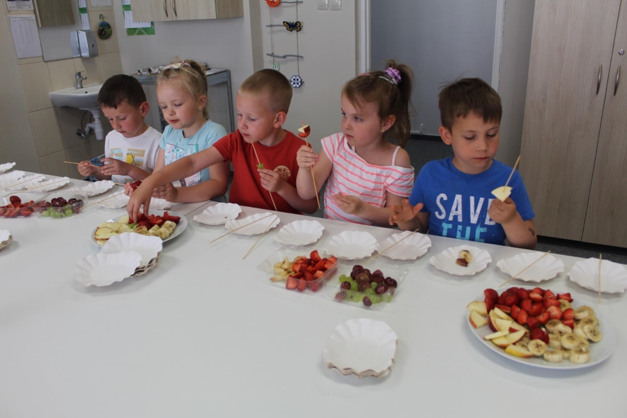 Grupa dzieci nawleka owoce na drewniane patyczki.