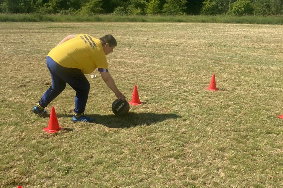 Uczestniczka turlająca piłkę między pachołkami.