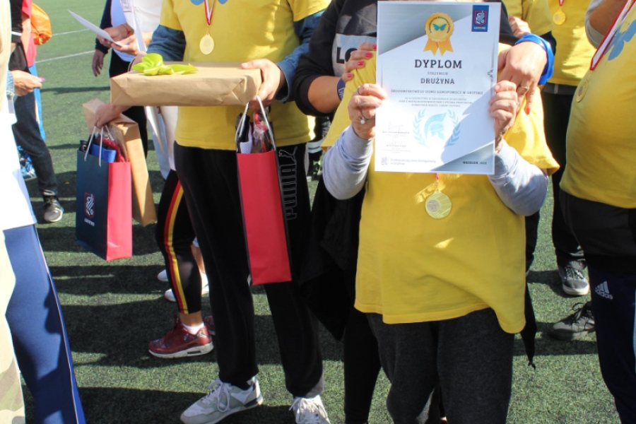 7. Uczestniczka pozuje do zdjęcia z dyplomem na tle grupy.