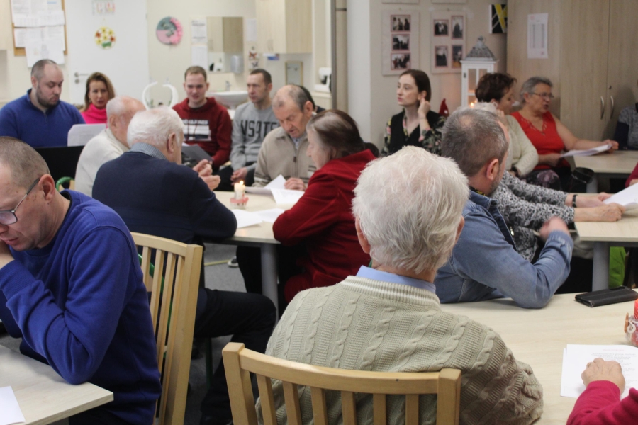 1.Grupa osób siedzących przy stołach śpiewających kolędy