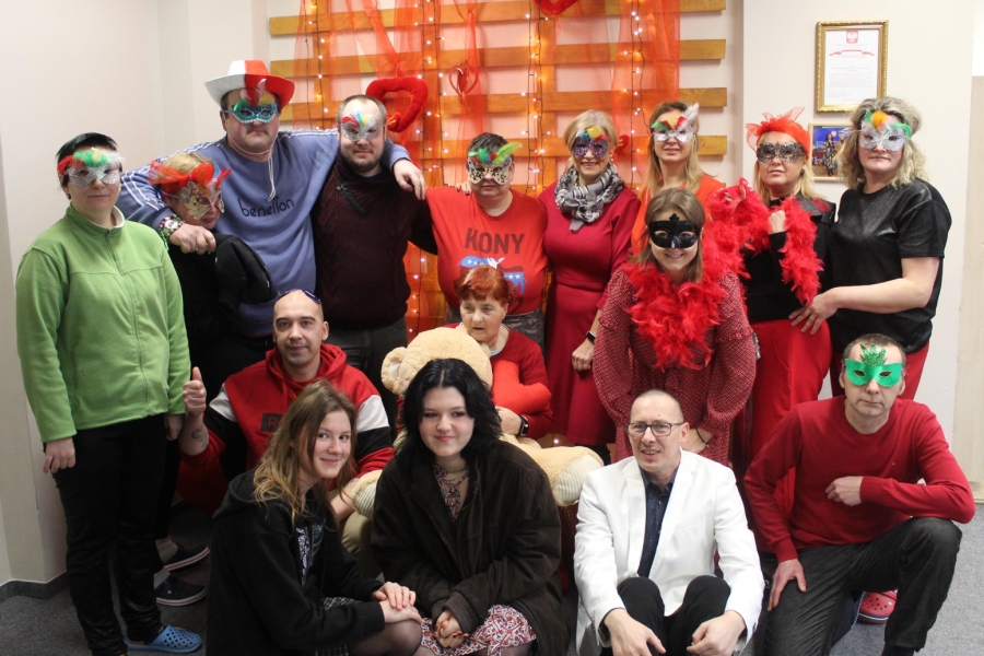 1.Uczestnicy oraz kadra ubrani na czerwono w maskach karnawałowych pozujący do zdjęcia grupowego na tle czerwon