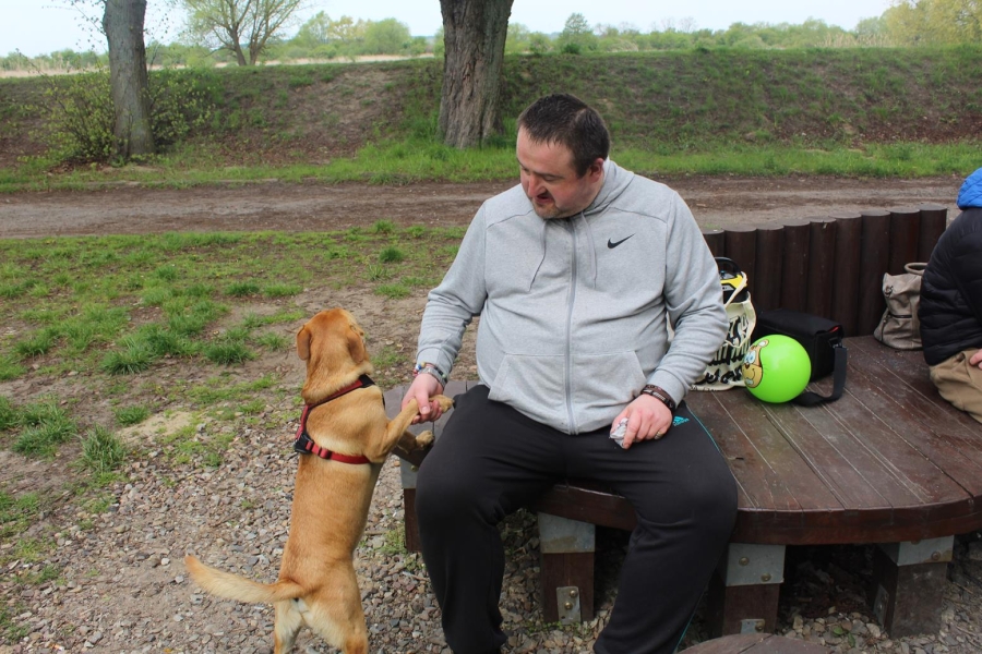 4.Uczestnik siedzący na drewnianej ławce, głaskając psa