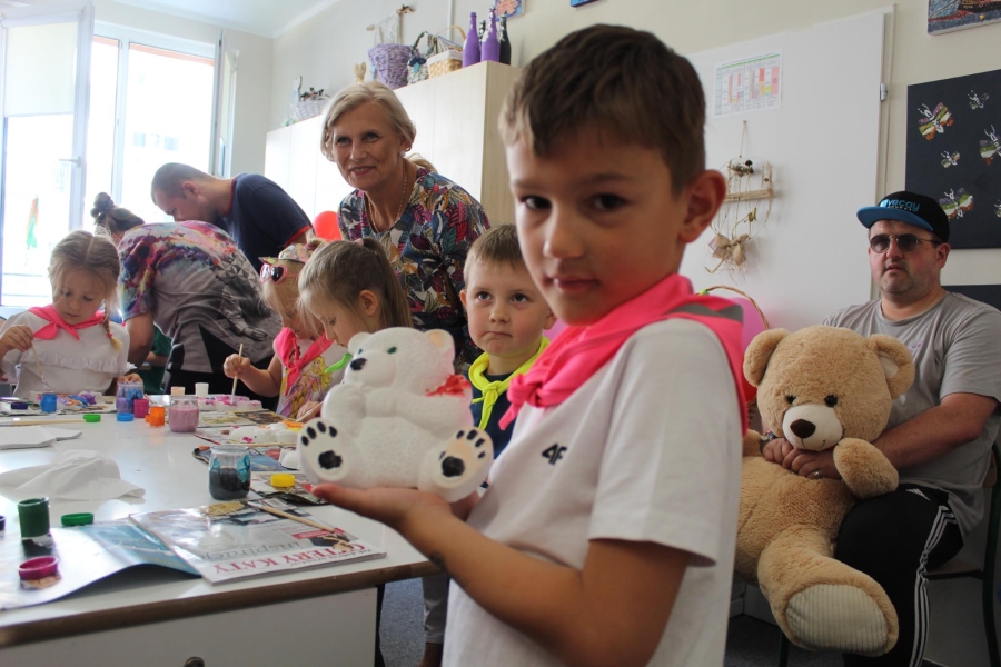 5.Chłopiec prezentujący pomalowanego gipsowego misia na tle innych dzieci oraz Pani Kierownik