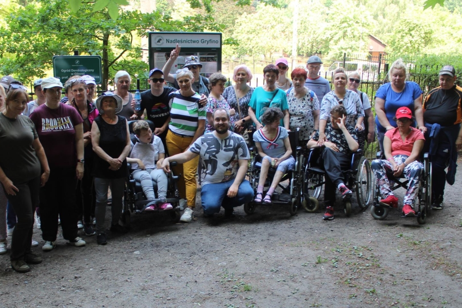 1.Grupa uczestników, terapeutów oraz  rodziców na tle wejścia do ogrodu dendrologicznego