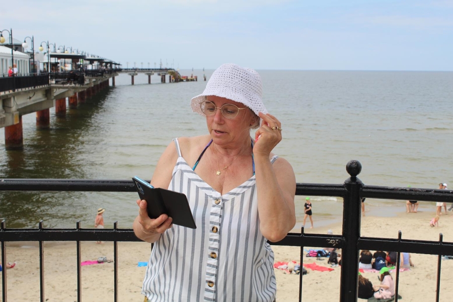 3.Uczestniczka trzymająca kapelusz na tle morza oraz molo