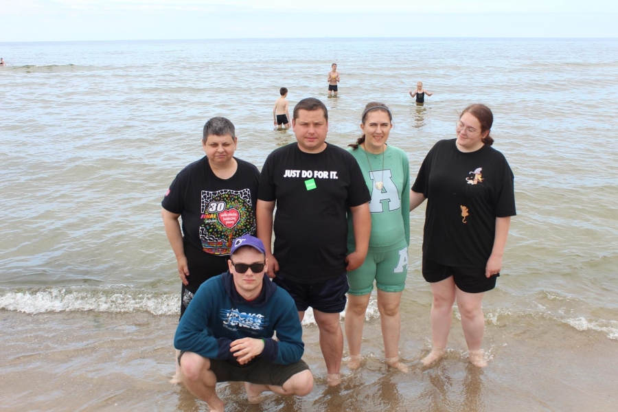8.Uczestnicy oraz Pani Wolontariusz stojący w płytkiej wodzie na tle morza