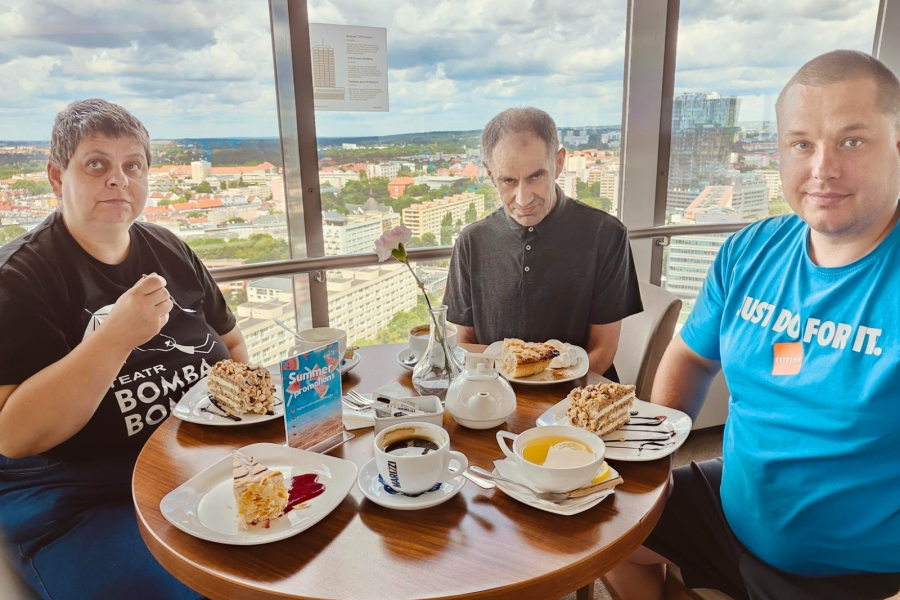 1.Uczesniczka oraz dwoje uczestników siedzący przy stole z kawą na tle panoramy szczecina