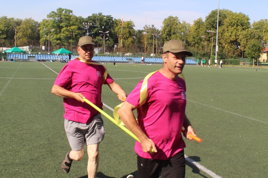 22.Zawodnicy spartakiady biegną trzymając żółte tyczki