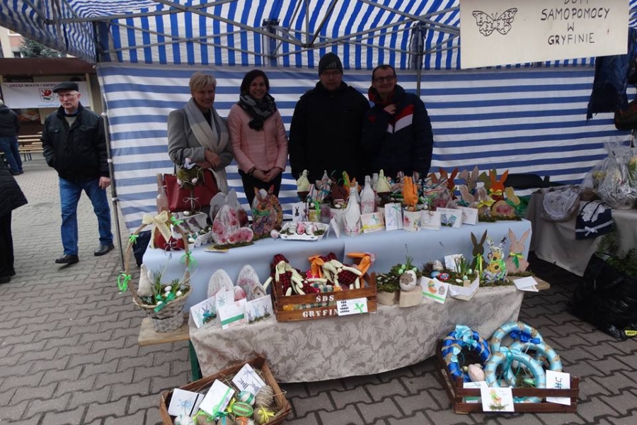 Uczestnicy wraz kadrą na tle stoiska z pracami wielkanocnymi