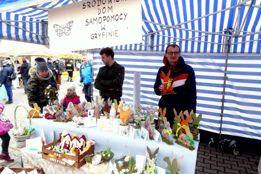 Uczestnik wraz z terapeutą na tle stoiska z pracami wielkanocnymi