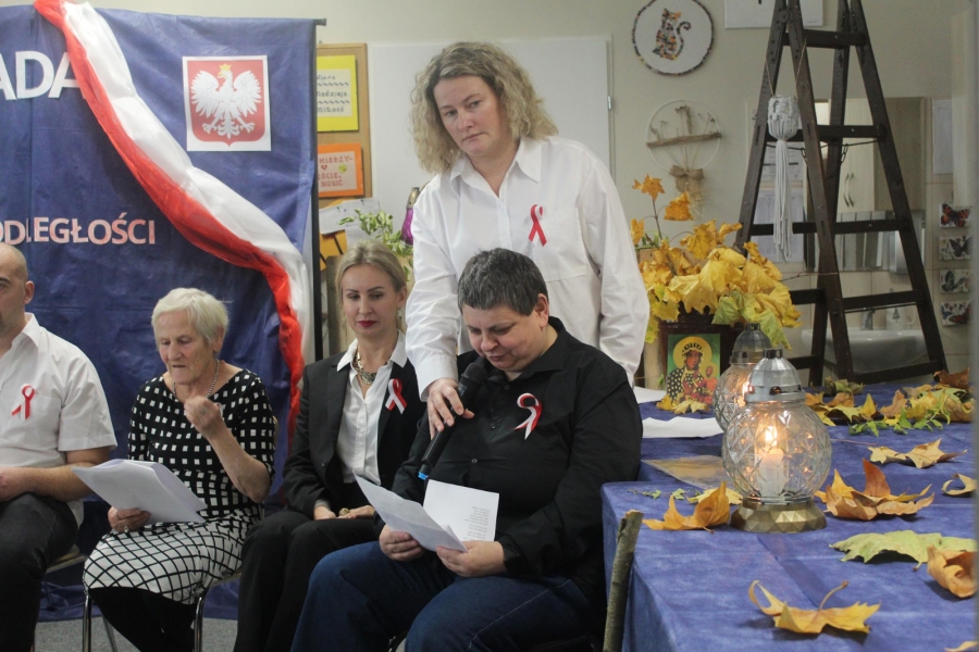 8.Uczestniczka mówiąca do mikrofonu na tle zniczy oraz rozrzuconych liści