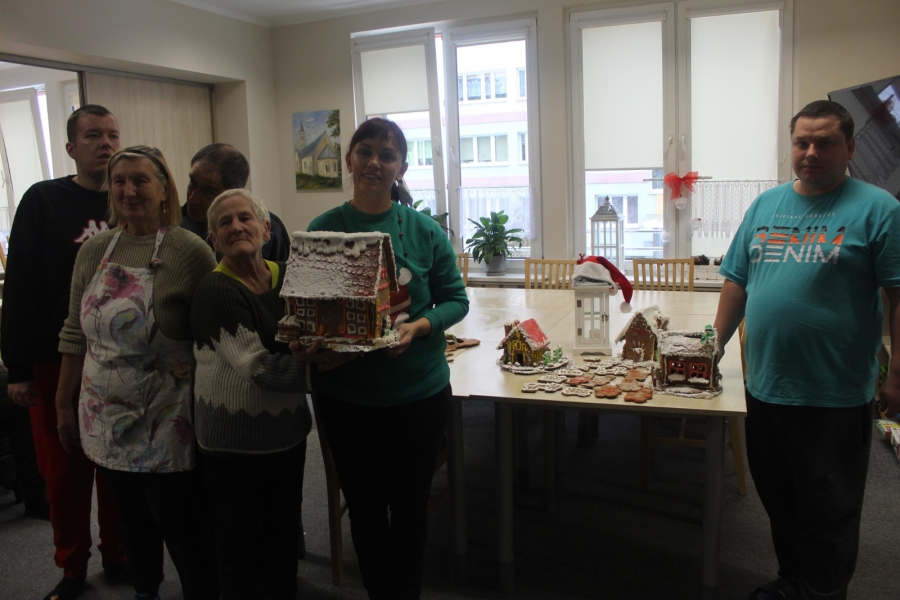 1.Uczestnicy oraz Pani Wolontariusz trzymająca domek na tle pozostałych domków z piernika