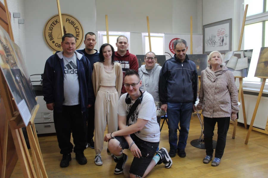 1.Fotograf oraz grupa uczestników stojący na tle wyeksponowanych fotografii