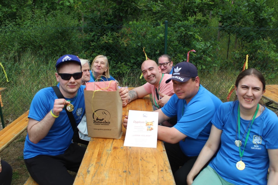 9.Uczestnicy przy drewnianym stole uśmiechający się do zdjęcia prezentując medale.