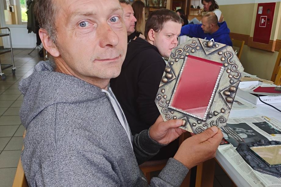 1.Uczestnik w szarej bluzie prezentujący wykonaną własnoręcznie ramkę na zdjęcia