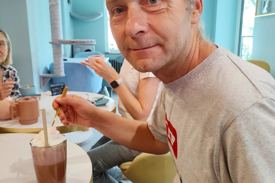 3.Uczestnik uśmiechający się przy kawie na tle niebieskiej ściany i zabawek dla kotów