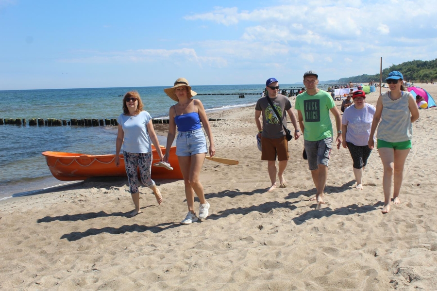 2.Uczestnicy oraz pedagog spacerujący brzegiem plaży na tle morza 