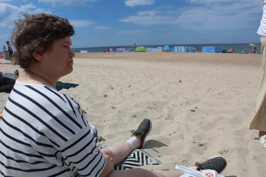 8.Uczestniczka siedząca na kocu na plaży patrząca w stronę morza