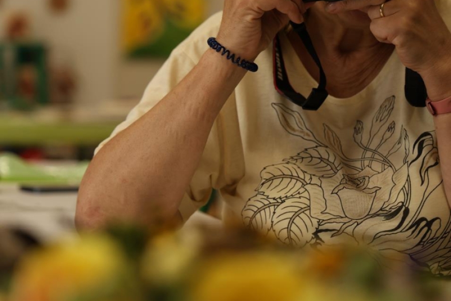 3.Rozmazane kwiaty na tle uczestniczki trzymającej aparat przy twarzy