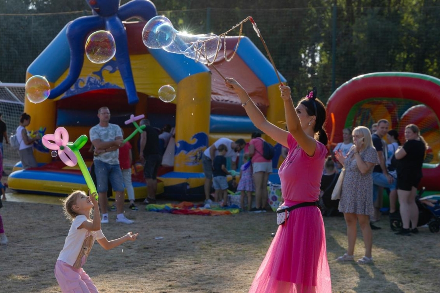 5.Pani w różowej sukience puszczająca bańki na tle kolorowych namiotów