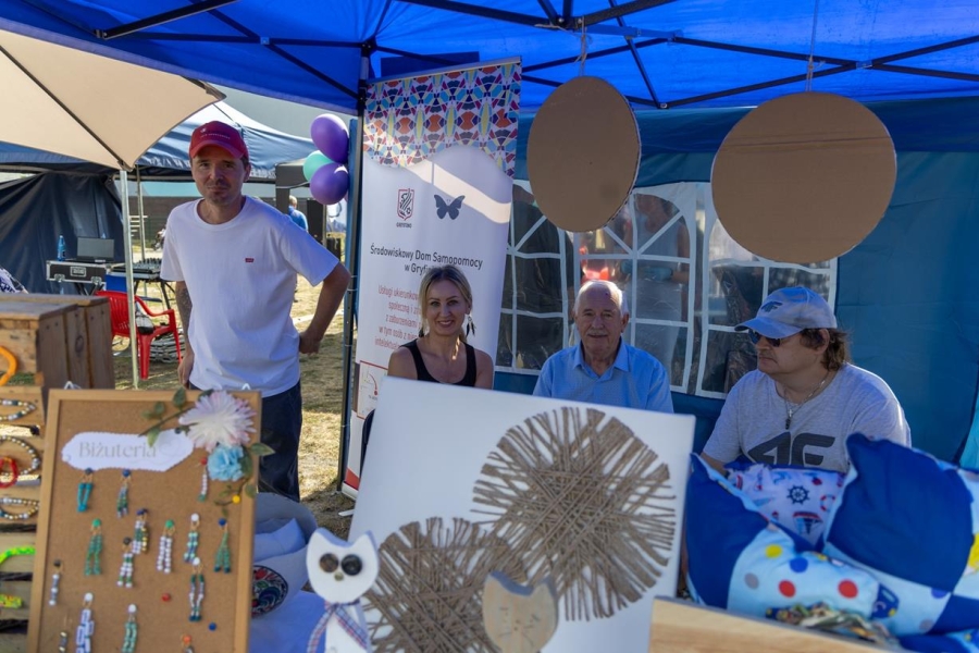 2.Kadra ŚDS w Gryfinie, uczestnik oraz starszy Pan na stoisku ŚDS w Gryfinie na tle rękodzieła