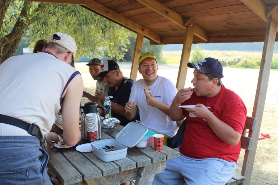2.Śmiejący się uczestnicy jedzą ciasto pod drewnianą altaną