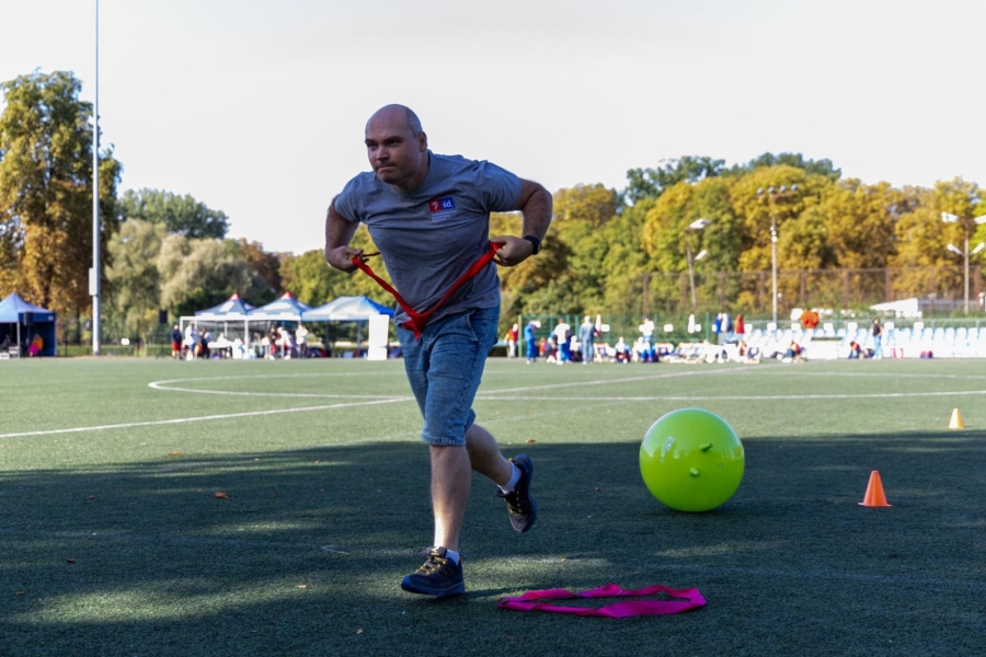 7.Biegnący uczestnik w szarej koszulce na tle boiska piłkarskiego