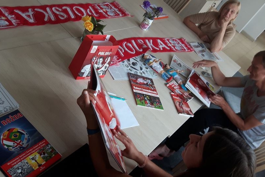 Terapeutka wraz z uczestnikami przeglądająca prasę sportową przy stole