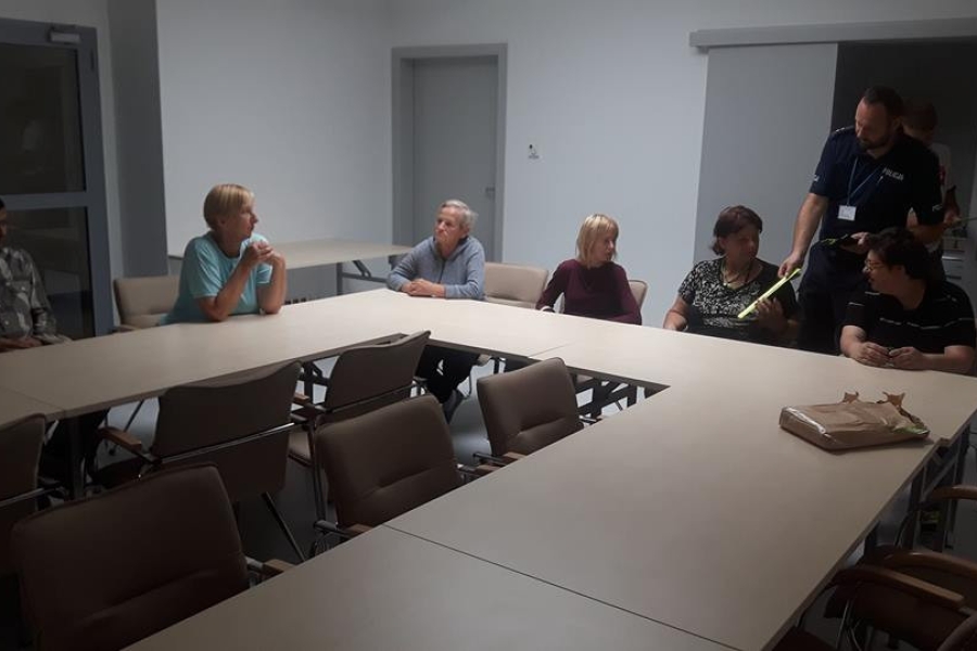 Grupa uczestników siedzących przy stole, słuchająca przemowy policjanta