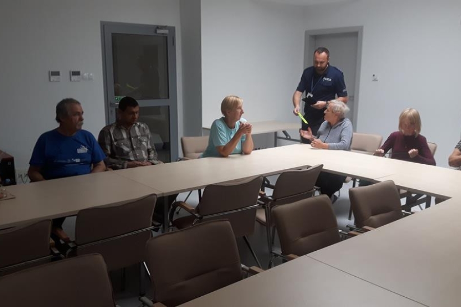 Grupa uczestników siedzących przy stole, słuchająca przemowy policjanta