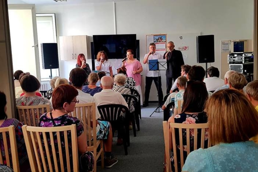 Goście oraz uczestnicy siedzący na krzesłach, słuchający występu muzycznego