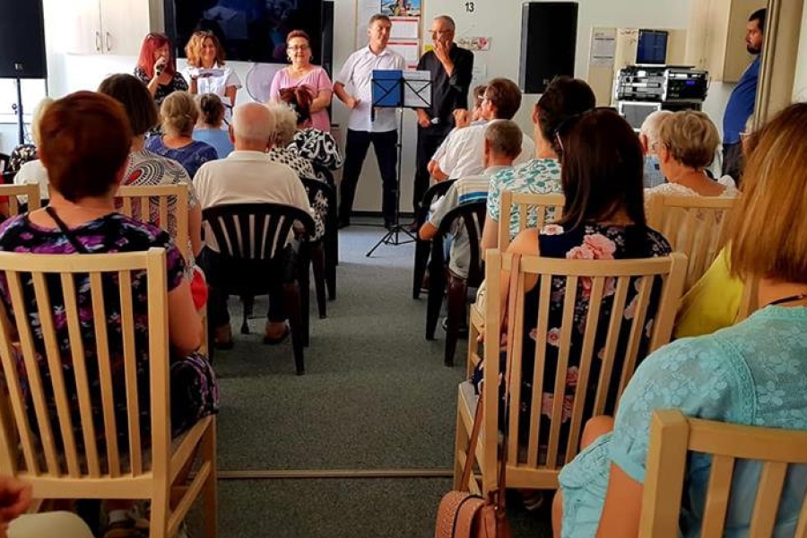 Goście oraz uczestnicy siedzący na krzesłach, słuchający występu muzycznego