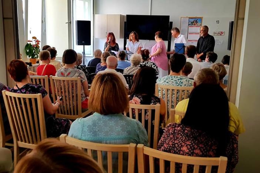 Goście oraz uczestnicy siedzący na krzesłach, słuchający występu muzycznego