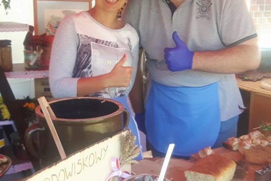 Uczestnik wraz z terapeutką trzymający kciuk w górze przy stoisku z wyrobami