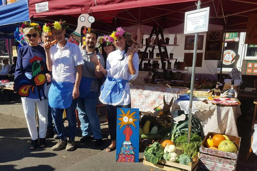 Pani Kierownik ŚDS z uczestnikami oraz kadrą na tle stoiska z wyrobami
