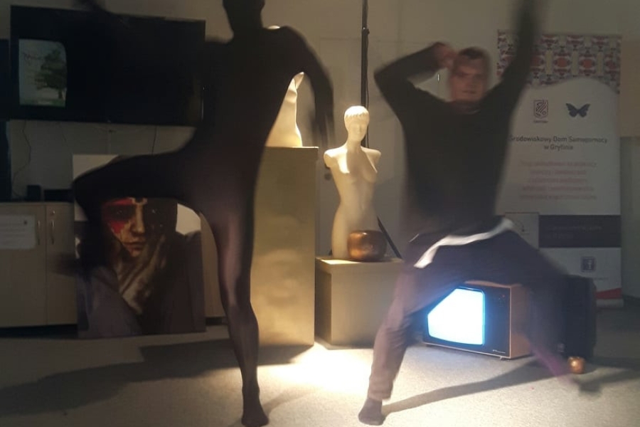 Aktorzy wykonujący figury na tle rekwizytów