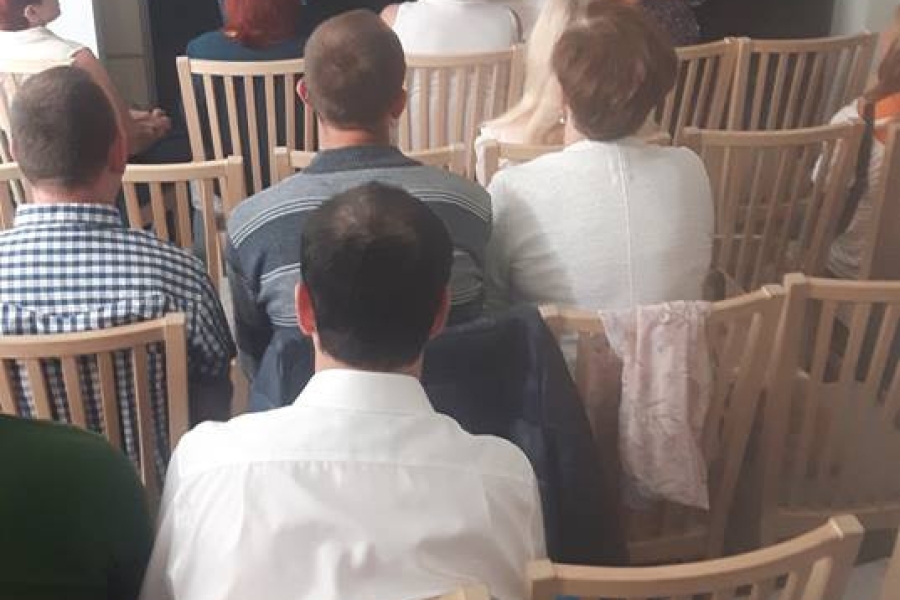 Uczestnicy wraz z gości siedzący na krzesłach podziwiający sztukę