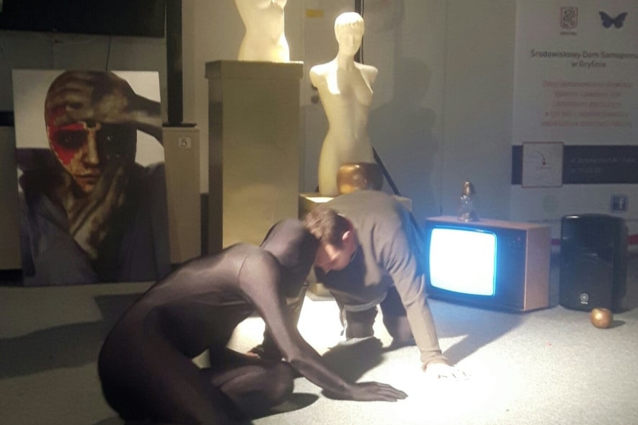 Aktorzy raczkujący po podłodze na tle rekwizytów