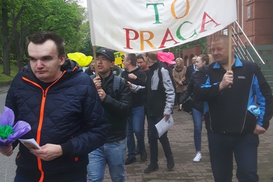 Uczestnicy niosący transparent „Godności to praca”