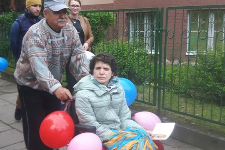 Uczestnik wiozący uczestniczką na wózku na tle budynków